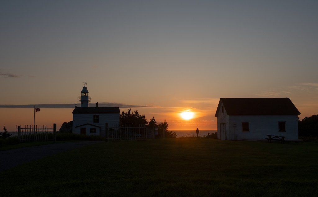 The silhouette of a man contemplating the sunset at Lobster Cove Head Lighthouse, Gros Morne National Park, Newfoundland, Canada